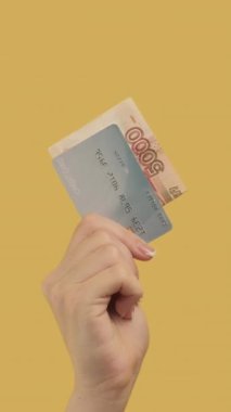 Dikey video. Nakit para transferi. Banka operasyonu. Ruble kredi kartı seti olan kadın eli sarı üzerine dört para hareketi yapıyor..