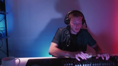 Gece oyunları. Sanal spor. Klavye yazma yarışmasına katılan etkileyici erkek, karanlık neon ışıklı ev iç mekanında oturuyor..