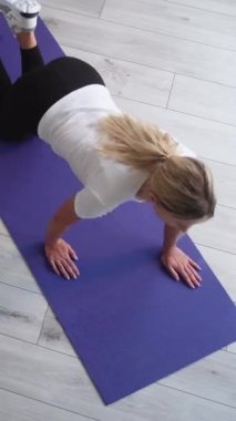 Dikey video. Evde eğitim. Kapalı spor salonu. Sportif kadın yoga minderi üzerinde şınav çekiyor. İç mekânda sağlıklı bir vücut bakımı..