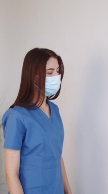 Dikey video. Yorgun doktor. Profesyonel yorgunluk. Zor bir gündü. Bitkin düşmüş, üniformalı, koruyucu maskeli kadın doktor yerde mola veriyor..