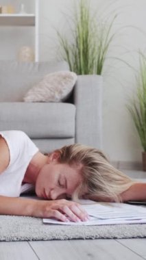 Dikey video. Çok çalışan serbest çalışan biri. Online iş. Yorgun kadın yönetici dizüstü bilgisayarlı kağıt grafiklerle yerde uyuyakalıyor. İç mekanda dinlenirken yorgunluk hissediyor..