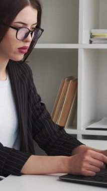 Dikey video. Ofis işleri. Serbest çalışmakla meşgul. Çevrimiçi iletişim. İç mekânda dizüstü bilgisayarda uzaktan kumanda kullanan konsantre olmuş ciddi bir kadın..