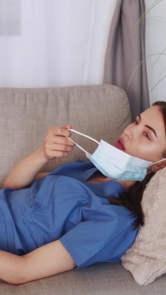 垂直录像 精疲力尽的医生医学专业 疲惫的女人躺在员工房间的沙发上 摘下防护面具灯房间的内部 — 图库视频影像