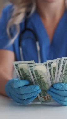 Dikey video. Doktor Cash. Sağlık sigortası. Sağlık sigortası kârı. Eldivenli tanınmayan kadın doktor 100 Amerikan doları sayıyor..