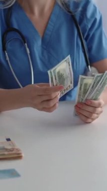 Dikey video. Doktor kazancı. Pahalı sağlık hizmeti. Tanınmayan kadın doktor para sayıyor. Amerikan doları iş yerinde nakit para basıyor..