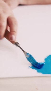 Dikey video. Soyut resim. Boyama işlemi. Yaratıcı stüdyo. Tuvale spatula ve mavi boyalarla resim çizen tanınmayan bir kadın..