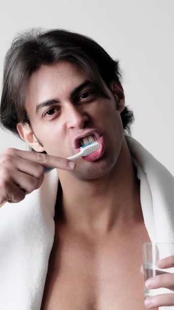 垂直ビデオ 歯を磨く 口腔ケア ハンサムな服男白いタオル上肩保持ガラス水歯ブラシ手順 — ストック動画