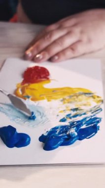 Dikey video. Sanat stüdyosu. Kadın ressam. Yaratıcı süreç. Renkleri karıştıran tanınmayan bir kadın, tablo tuvali ile spatula arasında soyut bir tablo oluşturur..