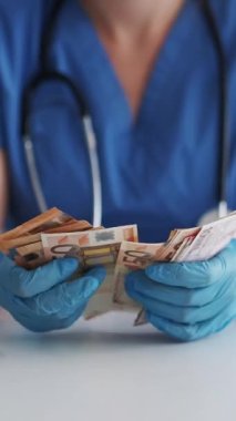 Dikey video. Doktor Cash. Sağlık sigortası. Sağlık sigortası masrafı. Avro banknotları sayan eldiven giymiş tanınmayan bir kadın pratisyen..