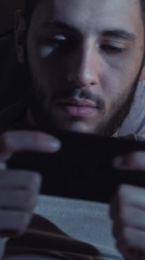 Dikey video. Gezici oyun. Gece keyfi. Uykusuzluk teknolojisi. Yatakta cep telefonu kullanan yorgun ve huzursuz bir adam..