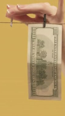 Dikey video. Para aklama. Offshore bankacılık. Kadın elleri sarı arka planda temiz dolar çıkarıyor..