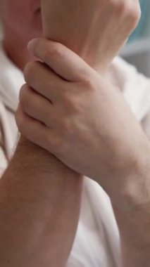 Dikey video. Ağrılı eklemler. Yaşlı adam. Yaş değişir. Tanımlanamayan yaşlı erkek masajcı eller uyuşmuş bir şekilde kanepede oturuyor..