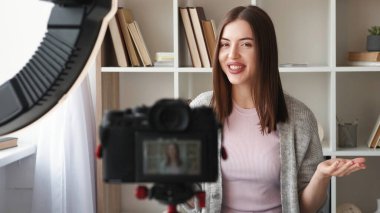 Video günlüğü. Çevrimiçi koçluk. Çekici, mutlu kadın blogcu internet içeriği yaratıyor. Tripod halka ışıklı ev iç mekanında konuşma kaydı yapıyor..