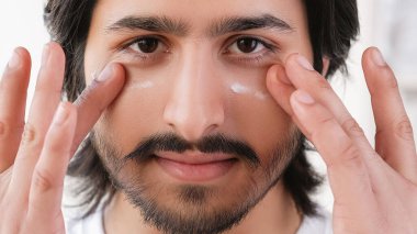 Erkek temizlik kremi. Cilt bakımı. Sakallı, kendine güvenen çekici bir adam. Yüzüne nemlendirici sürüyor. Işıklandırma odasında estetik ameliyatlar yapıyor..