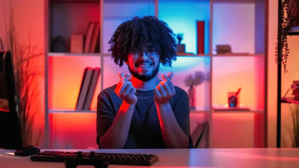 Small heart gesture. Positive man. Hand expression. Happy guy sending love message with finger sign sitting desk dark neon light room interior.