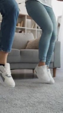 Dikey video. Hayatın tadını çıkarıyorum. Aile eğlencesi. Komik eğlence. Tanımlanamayan bir adam ve iki kadın dans ediyorlar. Evlerinin içinde birlikte atlıyorlar..