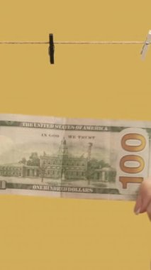 Dikey video. Para aklama. Ticari işlem. Kadın elleri sarı arka planda kuruması için dolar sallıyor..