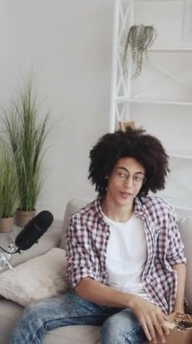 Dikey video. Telefon açılıyor. Teknik video günlüğü. Elektronik inceleme. Neşeli blogcu adam modern ev stüdyosunun içinde mikrofona konuşan alet kayıt içeriğini açıyor..