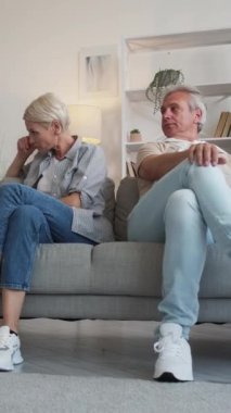 Dikey video. Aile içi anlaşmazlık. Kavga eden bir çift. Kızgın orta yaşlı adam ve kadın koltukta oturuyor ve evlerinde birbirlerini geri çeviriyorlar..