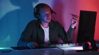 Gece oyunları. Çevrimiçi turnuva Siber rekabet. Kulaklıklı rahat bir adam bilgisayarına para ödüyor pizza yiyor boş zamanların tadını çıkarıyor karanlık neon ışıklı oda.