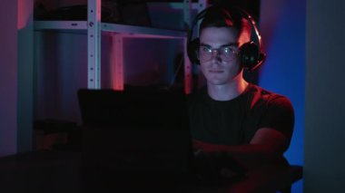 Serbest bir iş. Yazılım geliştirme. Gözlüklü ve kulaklıklı kendinden emin erkek programcı gece evde dizüstü bilgisayar kullanarak proje üzerinde çalışıyor..