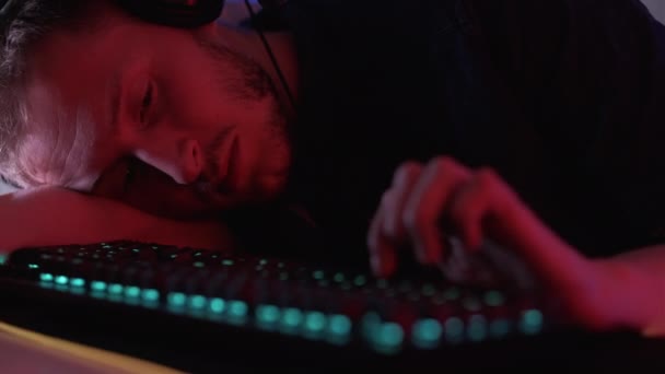 退屈ゲーマー 眠いプログラマー 疲れたハッカー 疲れ男はゆっくりと入力テーブルの上に傾いた緑のバックライトキーボード眠りに落ちながらチャットでストリーム — ストック動画