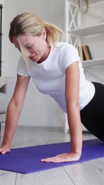 Dikey video. Kapalı alanda egzersiz. Evde fitness. Güçlü atletik güdümlü kadın vücut bakımı egzersizi yapıyor. Vücut bakımı, pazıların iç kısımlarını eğitiyor..