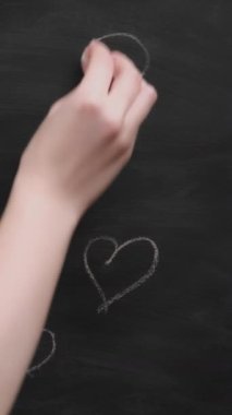 Dikey video. Aşk işaretleri. Romantik mesaj. Kadın eli tahtaya farklı boyutlarda kalp çiziyor..