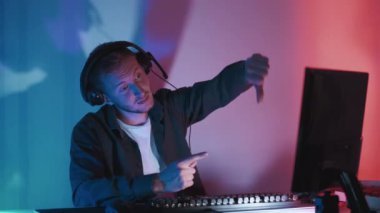 Hayal kırıklığına uğramış oyuncu. Nefret dolu bir jest. Kulaklık takmış yetişkin bir adam çevrimiçi oyun işaretleme monitörüyle başparmaklarını göstererek sorunsuz döngü gösterir.