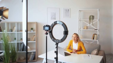 Çevrimiçi koçluk. İş videosu. Canlı yayın. Gülümseyen başarılı kadın konuşmacı ev içini açıklayan video dersi alıyor..