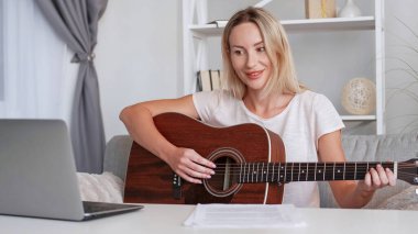 Online gitar dersi. Müzik öğretmeni. Gülümseyen kadın öğretmenlik dersleri ev içi dizüstü bilgisayarda eğitim videosu kaydederek enstrüman çalmayı öğretiyor.