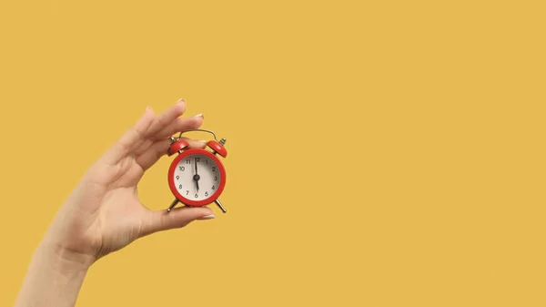 Time management. Progress achievement. Woman hand holding red alarm clock on yellow background copy space.