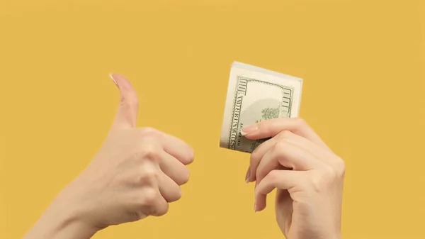 Passive income. Agreed gesture. Woman hands showing dollars and like sign d on orange yellow background.