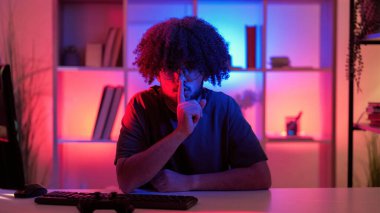 Sessiz ol. Sessiz adam. El hareketi. Hippi adam elinde şşşş parmağını ağzında tutuyor. Neon ışıklı odada masa başında oturuyor..