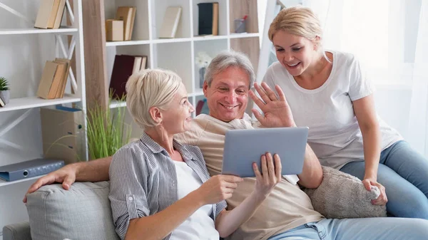 Çevrimiçi toplantı. Mutlu bir aile. Mesafe iletişimi. Pozitif anne-baba ve kızı tablet bilgisayardan arkadaşlarıyla selamlaşıyorlar..