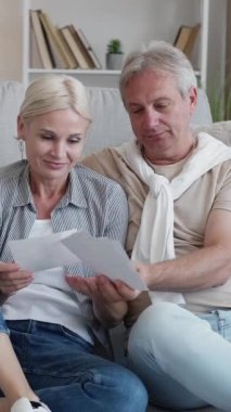 Dikey video. Fotoğraf hatıraları. Mutlu bir çift. Boş bir gün. Orta yaşlı bir adam ve kadın aile fotoğraflarına bakıyor. Açık bir evin içinde yerde birlikte oturuyorlar..