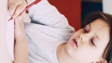 Dikey video. Çocuklar resim yapıyor. Sanat okulu. Yaratıcı zaman. Kağıt üzerine kalemle çizim yapan kız aydınlık odada oturuyor..