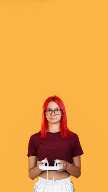 Müzik aleti. Modern bir alet. Güzel çağdaş tasarım telli gözlüklü genç kızıl kız ellerinde turuncu arka planda boş alan olan kulaklıklar..