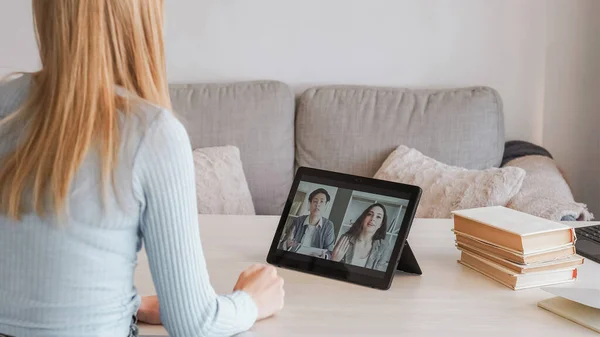 Video conference. Online teamwork. Remote business meeting. Back view of woman speak to multiethnic colleagues from home on tablet.