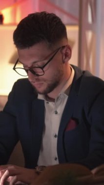 Dikey video. İş araştırması, meşgul adam. Çevrimiçi iletişim. Bilgisayarı daktilo eden zeki bir adam karanlık odanın içinde oturuyor..