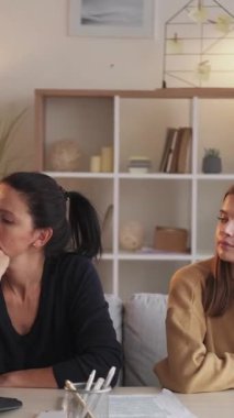 Dikey video. Aile kavgası. Ev içi çatışma. Gülümseyen anne genç kız, masa lambasının içinde oturup tartıştıktan sonra barış yapıyor..