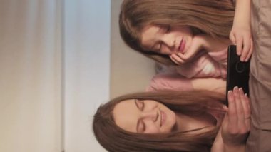 Dikey video. Çocuk e-öğrenimi. Aile çalışması. Online eğitim. Rahat anne, küçük kız telefonda sanal ders seyrediyor. Sabah yatak odasında boş yer var..