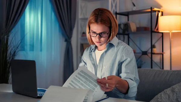 仕事の研究 忙しい女だ 遠隔教育 濃密な女性は暗い光の部屋のインテリアでノートパソコンと机に座ってドキュメントを勉強 — ストック写真