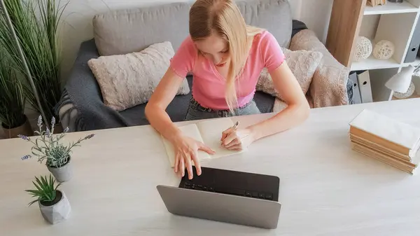 网上教育 学生作业 准备专业的 全神贯注的金发姑娘在家里的桌上用笔记本电脑写笔记 — 图库照片