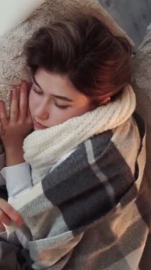 Dikey video. Hapşırma belirtileri. Mevsimsel grip. Hasta kadın kanepede yatarken soğuk algınlığı geçiriyor. Evde burun nezlesi geçiriyor..