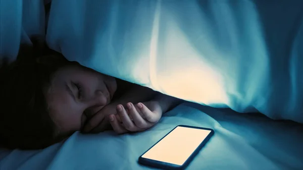 子供への執着 テクノロジー中毒 夜のソーシャルメディア 女の子は眠りに落ちたとともにホワイトロックされたスマートフォン空白のMokup画面でダークベッドルームに家空のスペース — ストック写真