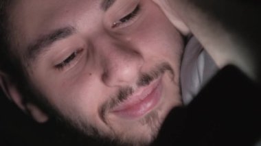 Gece filmi. Gece uykusu. Çevrimiçi eğlence. Rahatlamış adam telefonda komedi videosu izliyor. Karanlıkta yatakta yatıp gülüyor..