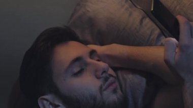 Dikey video. İnternet uykusuzluğu. Gece online. Gezici bağımlılık. Sıkıcı, uykulu, yorgun bir adam. Gece geç saatlerde, karanlık bir yatak odasında telefon kaydırağı kullanıyor..