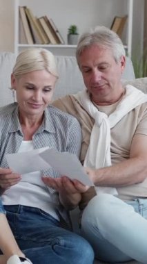 Dikey video. Fotoğraf hatıraları. Mutlu bir çift. Boş bir gün. Orta yaşlı bir adam ve kadın aile fotoğraflarına bakıyor. Açık bir evin içinde yerde birlikte oturuyorlar..