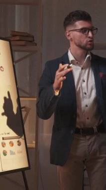 Dikey video. İş projesi. Erkek konuşmacı. Görsel sunum. Şirket geliştirme çalışmalarının sonuçlarını oda içinde gösteren ilham verici bir adam..